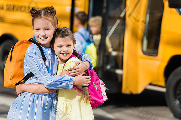 美丽的快乐女生相机拥抱前面学校公共汽车
