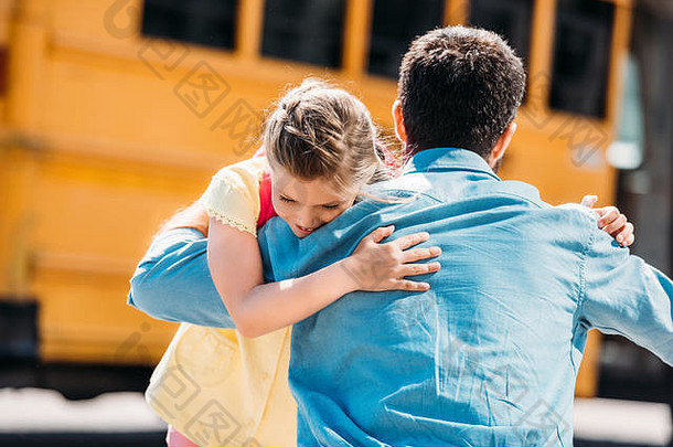 后视图父亲女儿拥抱前面学校公共汽车