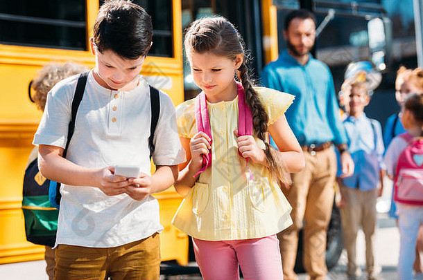 可爱的女学生小学生智能手机前面学校公共汽车同学们