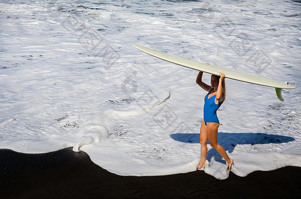 运动女孩比基尼冲浪董事会走黑色的沙子海滩年轻的冲浪者女人运行水池白色泡沫活跃的人体育冒险