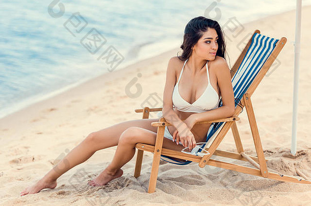 有吸引力的女孩持有太阳镜坐着海滩椅子海