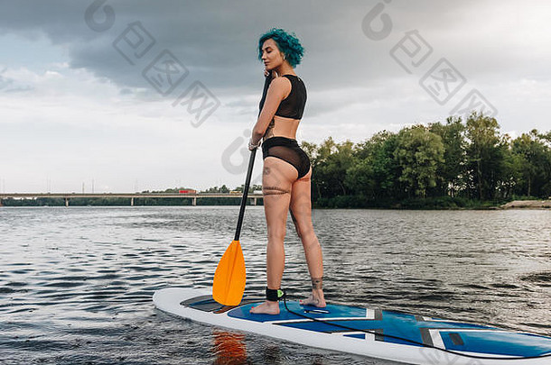有吸引力的纹身女人蓝色的头发站立会议paddleboarding河