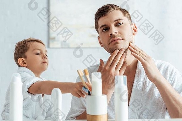 年轻的父亲触碰脸可爱的儿子采取牙刷