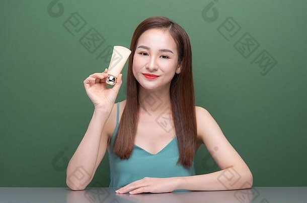 有吸引力的年轻的亚洲女人持有显示奶油管产品绿色背景
