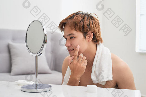年轻的亚洲男人。镜子检查皮肤