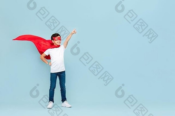 微笑超级英雄男孩红色的面具角指出手孤立的光蓝色的背景