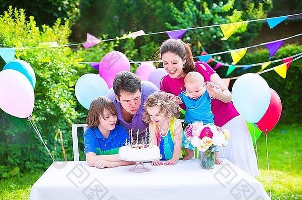 快乐大家庭孩子们享受生日聚会，派对蛋糕吹蜡烛花园装饰气球横幅