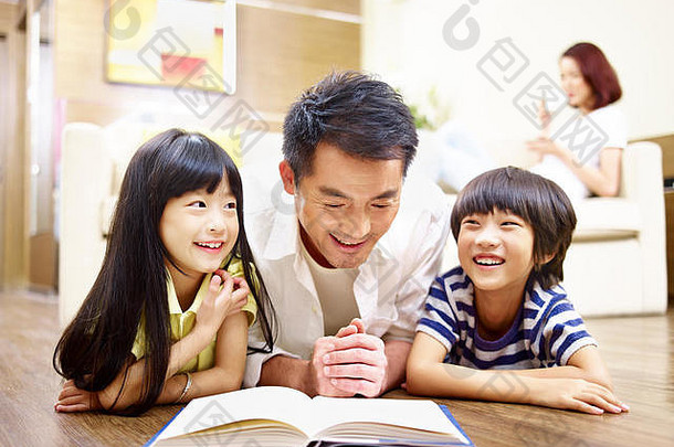 亚洲父亲孩子们说谎地板上阅<strong>读书</strong>妈妈。背景