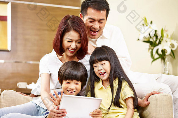 亚洲父母妈妈。父亲孩子们儿子女儿坐着家庭沙发上数字平板电脑