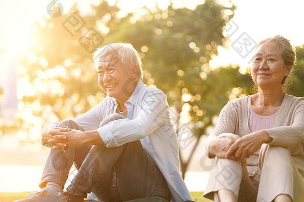 亚洲高级夫妇坐着草享受日落在户外公园