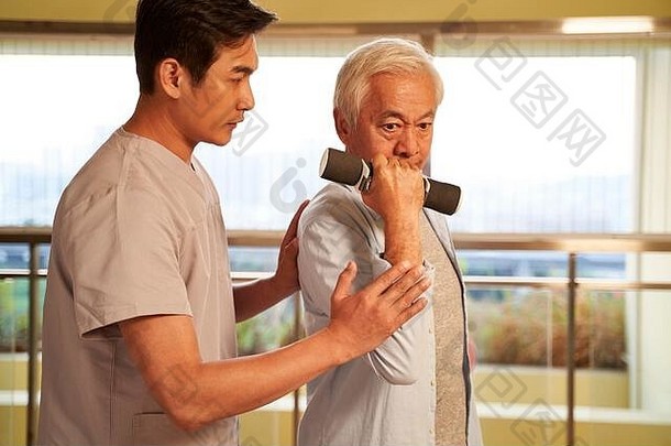 高级亚洲男人。锻炼哑铃引导物理治疗师康复中心