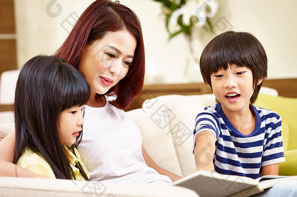 年轻的亚洲妈妈。儿子女儿坐着沙发上阅读书