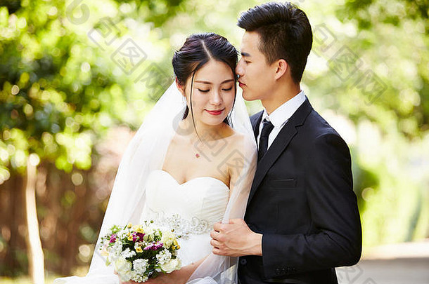 年轻的亚洲新郎接吻新娘在户外婚礼仪式