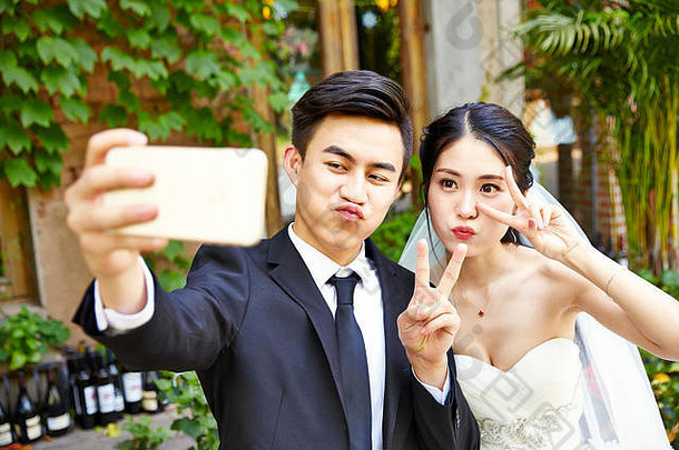 快乐年轻的亚洲新娘新郎使脸采取自拍手机