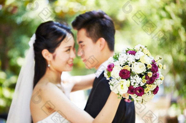 年轻的亚洲新结婚夫妇拥抱婚礼仪式焦点花束