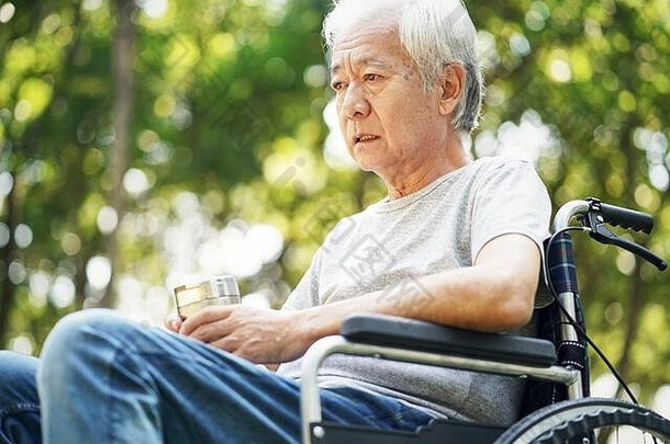 伤心亚洲高级男人。坐着在户外轮椅