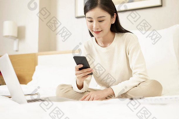 美丽的年轻的亚洲女人坐着<strong>床上</strong>工作移动电话移动PC电脑
