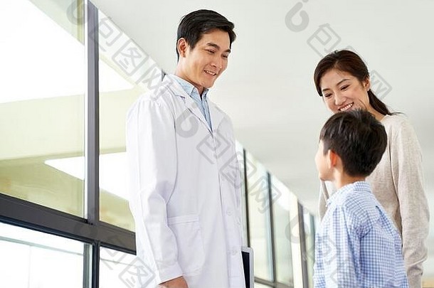 友好的年轻的亚洲儿科医生会说话的妈妈。儿子医院走廊