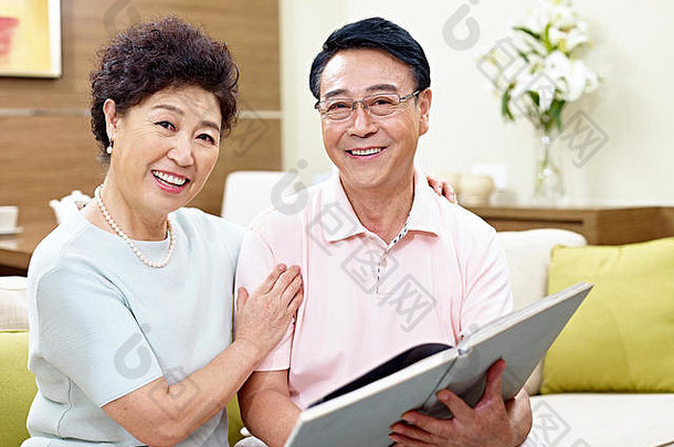 高级亚洲夫妇坐着沙发上相机书手快乐微笑