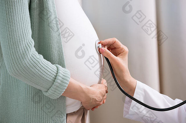 裁剪拍摄医生听诊器听肚子怀孕了女人