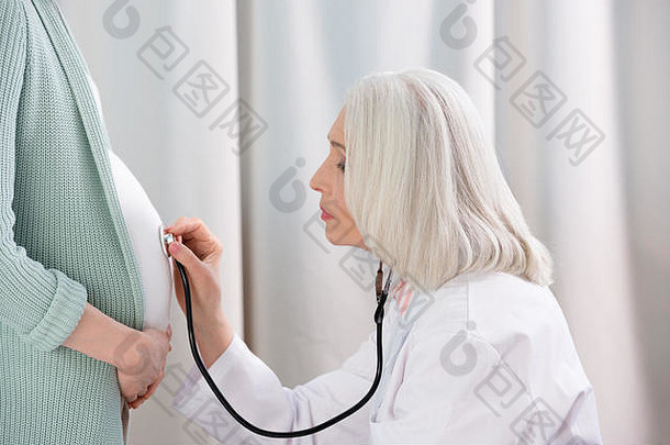 一边视图<strong>医生</strong>听诊器听肚子怀孕了女人