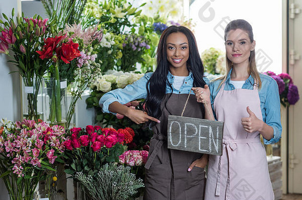 年轻的多民族花店指出开放标志显示拇指微笑相机花商店