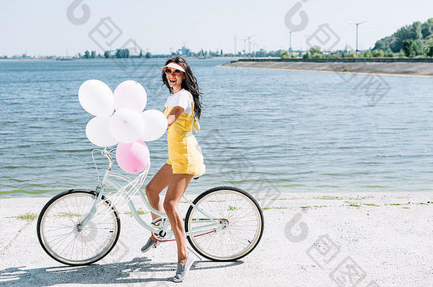 一边视图美丽的浅黑肤色的女人女孩骑自行车气球河