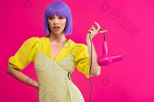 困惑流行艺术女孩紫色的假发持有头发干燥机孤立的粉红色的