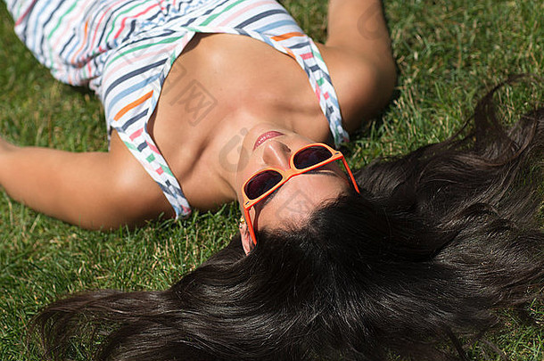 年轻的女人穿背心裙日光浴草坪上