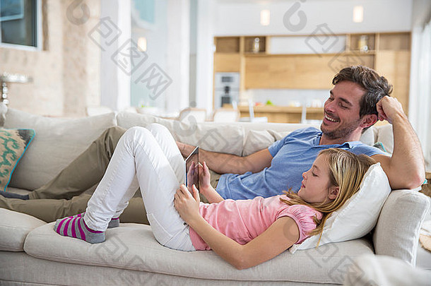成熟的男人。女儿倾斜的沙发浏览数字平板电脑