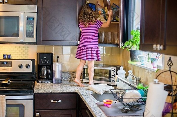 年轻的女孩站厨房工作表面对待橱柜后视图