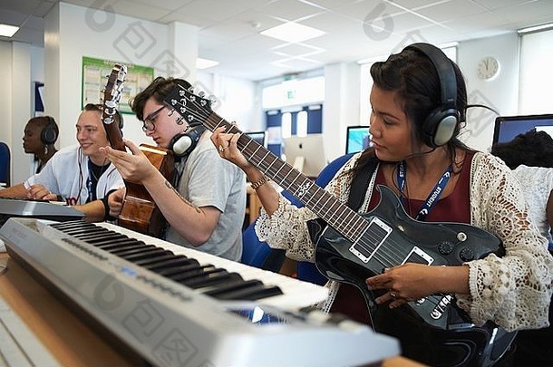 小集团大学学生坐着前面键盘穿耳机玩吉他