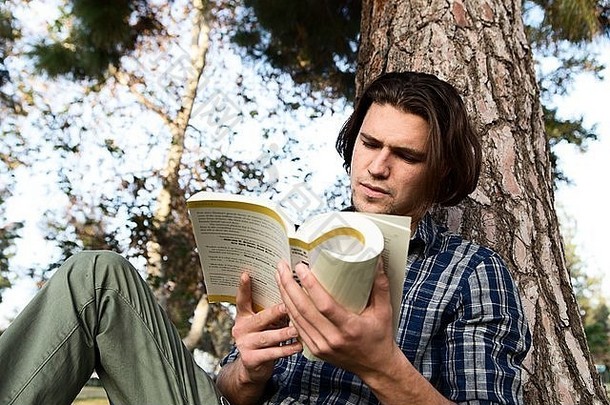 <strong>低</strong>角视图年轻的男人。坐着树阅读书