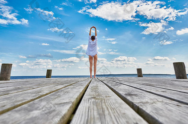 年轻的女人站木码头伸展运动后视图