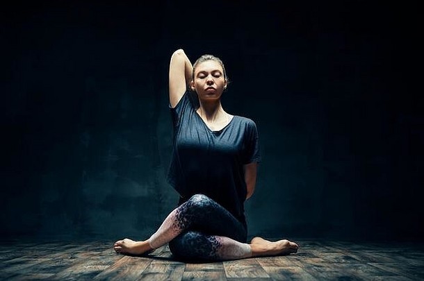 <strong>年轻的</strong>女人练习瑜伽戈穆哈萨那牛脸构成黑暗房间