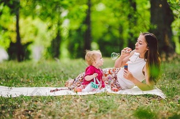 微笑女人玩坐绿色草公园休息拥抱持有肥皂泡沫鼓风机可爱的孩子婴儿女孩快乐