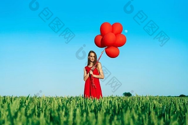 年轻的美丽的女人红色的衣服摆姿势绿色场红色的气球
