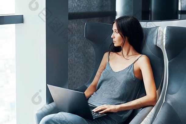 年轻的女人工作移动PC坐着大舒适的椅子现代室内