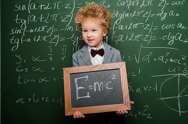 聪明的孩子西装弓领带持有小黑板上公式黑板