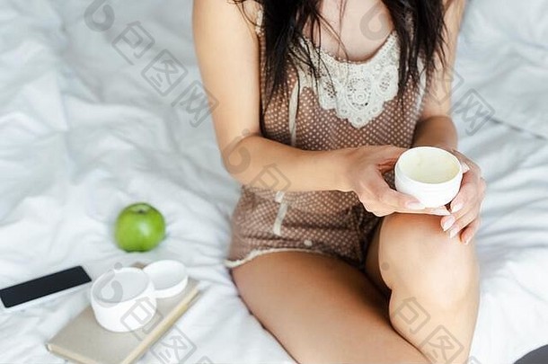 裁剪视图女人持有脸奶油坐着床上塑料容器智能手机苹果