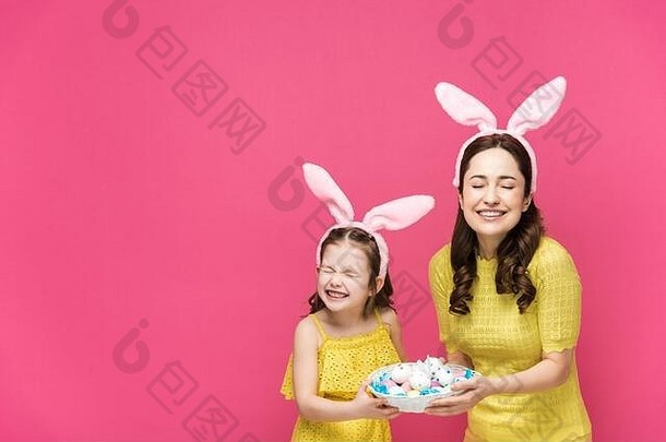 快乐妈妈。女儿兔子耳朵持有复活节鸡蛋笑孤立的粉红色的