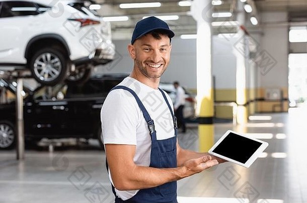 快乐的机械师工作服帽持有数字平板电脑空白屏幕车服务