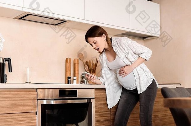 怀孕了女人触碰肚子抽筋持有智能手机厨房