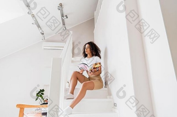 年轻的非洲美国女人坐着楼梯杂志