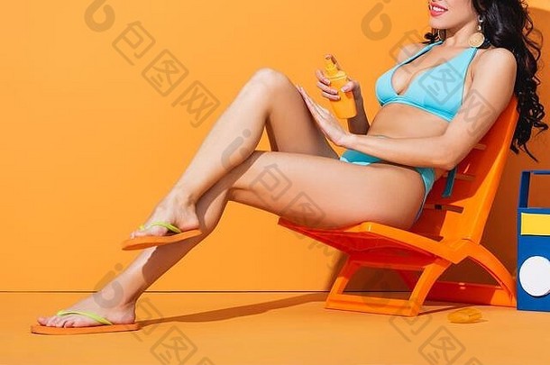 裁剪视图快乐女孩泳衣坐着甲板椅子应用防晒霜橙色