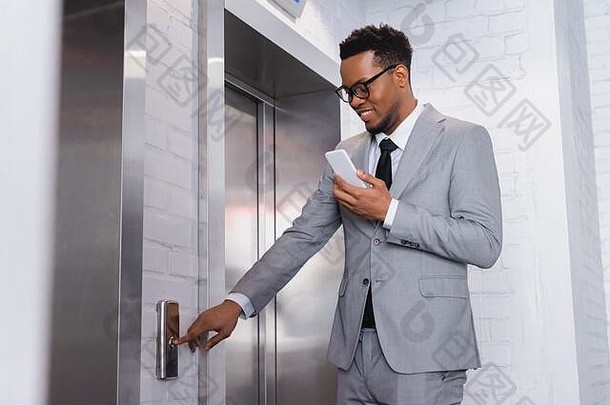 积极的非洲美国商人智能手机推电梯<strong>按钮</strong>