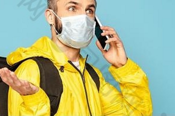 困惑送货人<strong>医疗</strong>面具黄色的统一的背包会说话的智能手机孤立的蓝色的