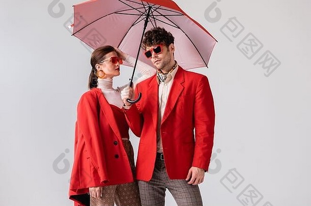 年轻的时尚夫妇红色的开拓者太阳镜摆姿势伞孤立的灰色