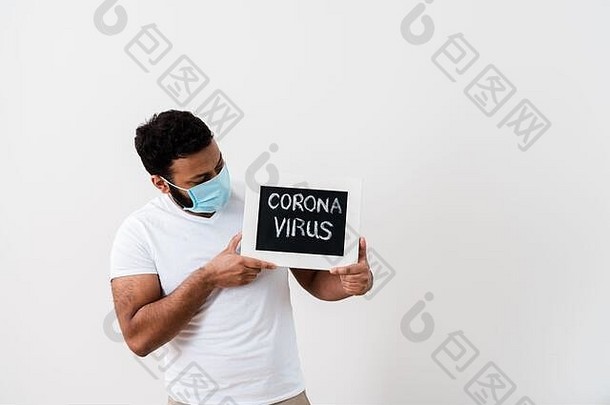 非洲美国男人。蓝色的医疗面具黑板冠状病毒刻字白色墙
