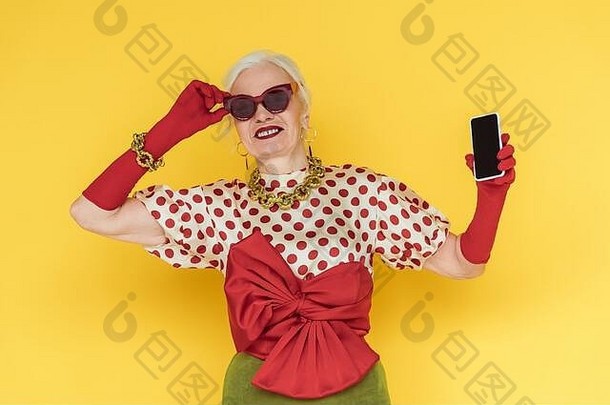 时尚的高级女人微笑持有智能手机空白屏幕黄色的背景